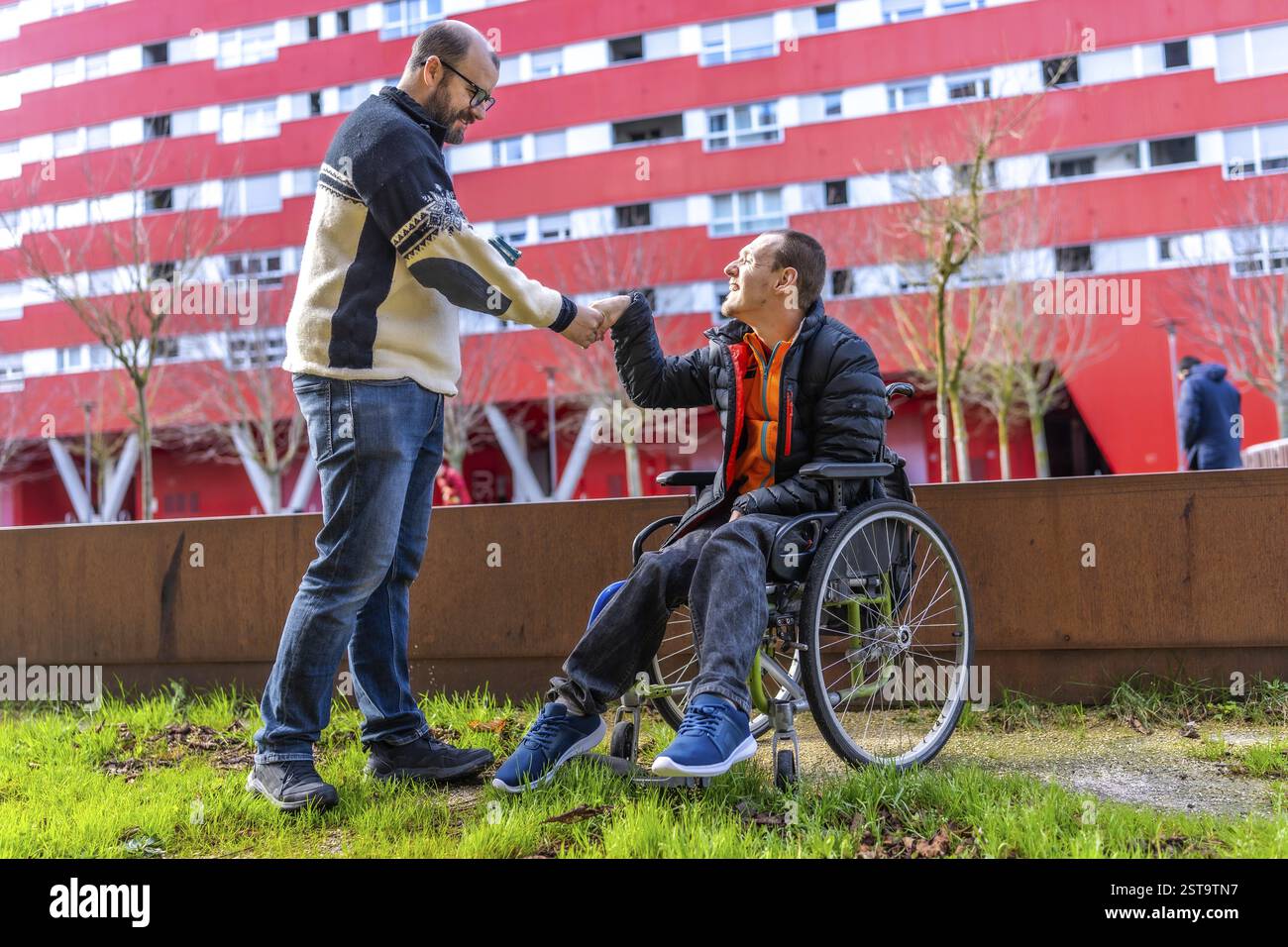 Two friends shaking hands in a city park, one of whom is using a ...