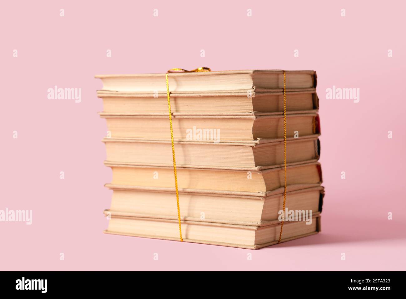 Stack of books with golden ribbon on pink background Stock Photo - Alamy