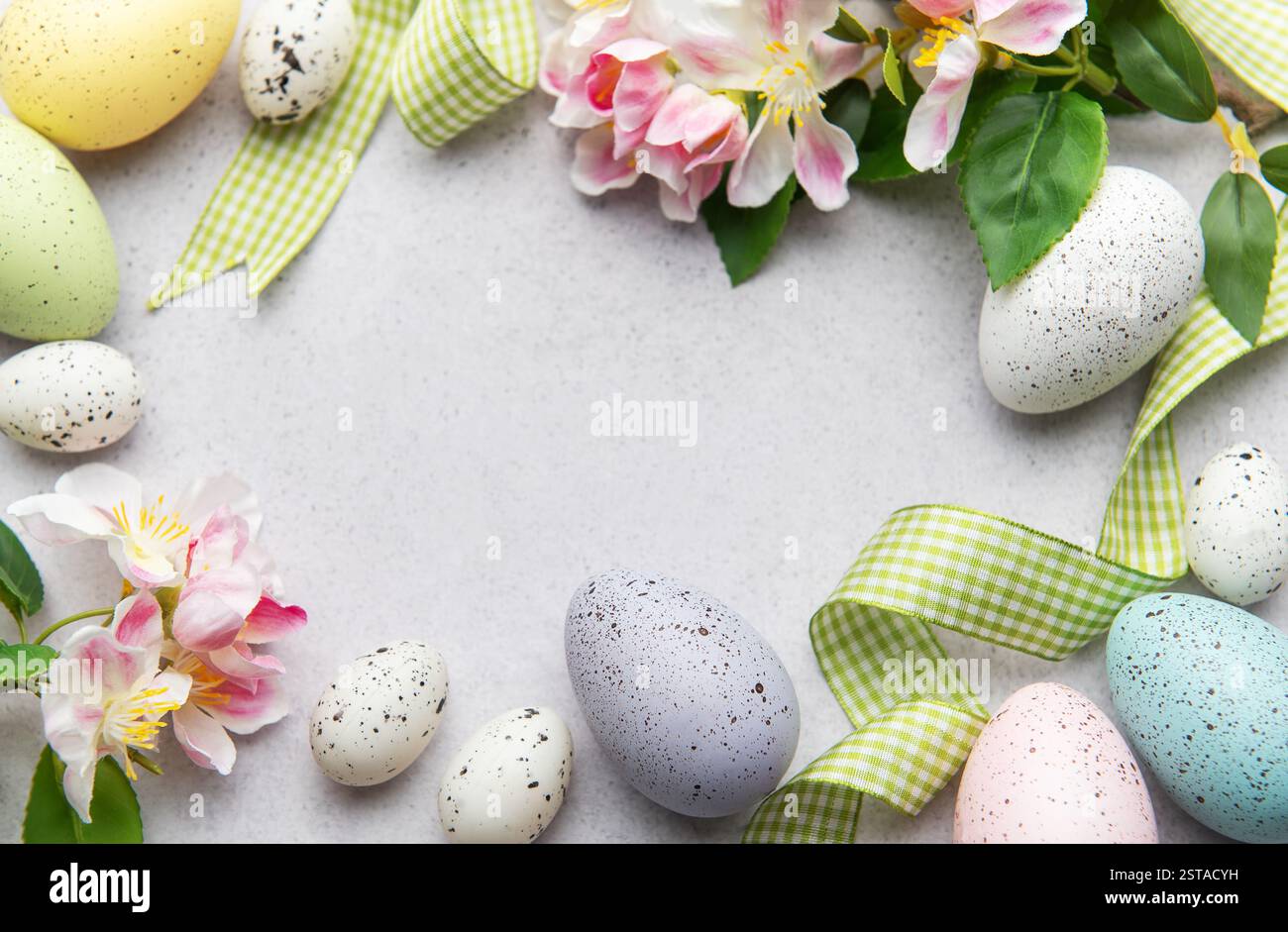 Easter eggs and spring flowers are creating a frame on a gray ...
