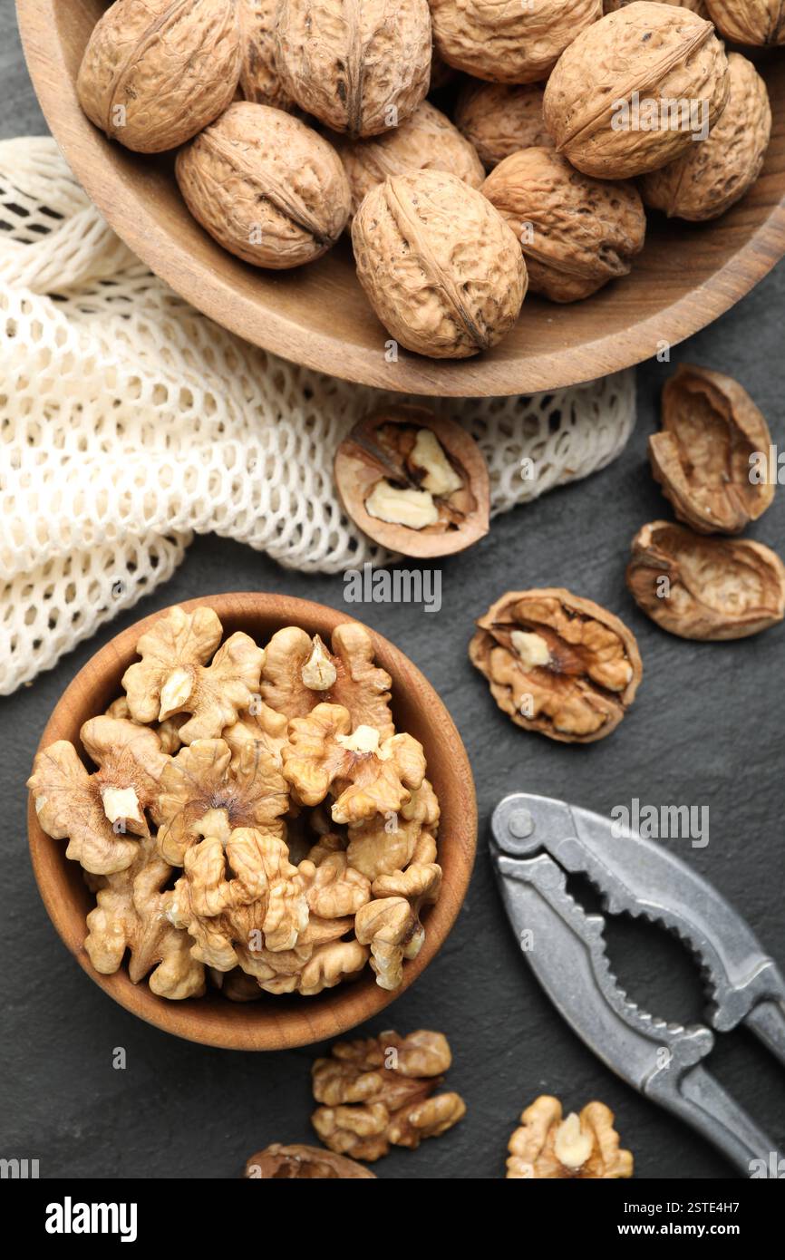 Fresh ripe walnuts, nutcracker and shells on black table, flat lay Stock Photo