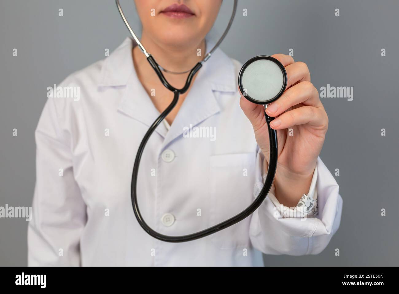 Anonymous healthcare worker in a white coat holds a stethoscope towards the camera, symbolizing medical examination and care Stock Photo