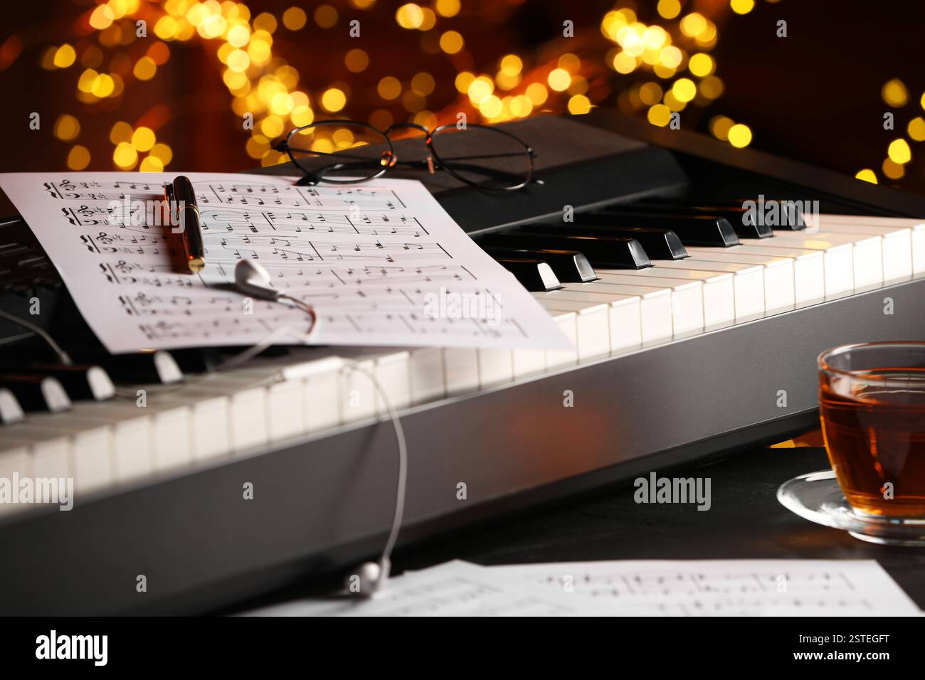 Piano, musical notes, pen and cup of tea on table against blurred lights, closeup. Bokeh effect Stock Photo
