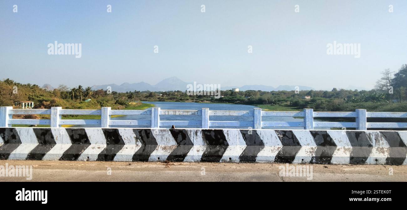 A scenic bridge stretching over a broad river, surrounded by lush greenery and a peaceful landscape. - Smartphone Captured Stock Image