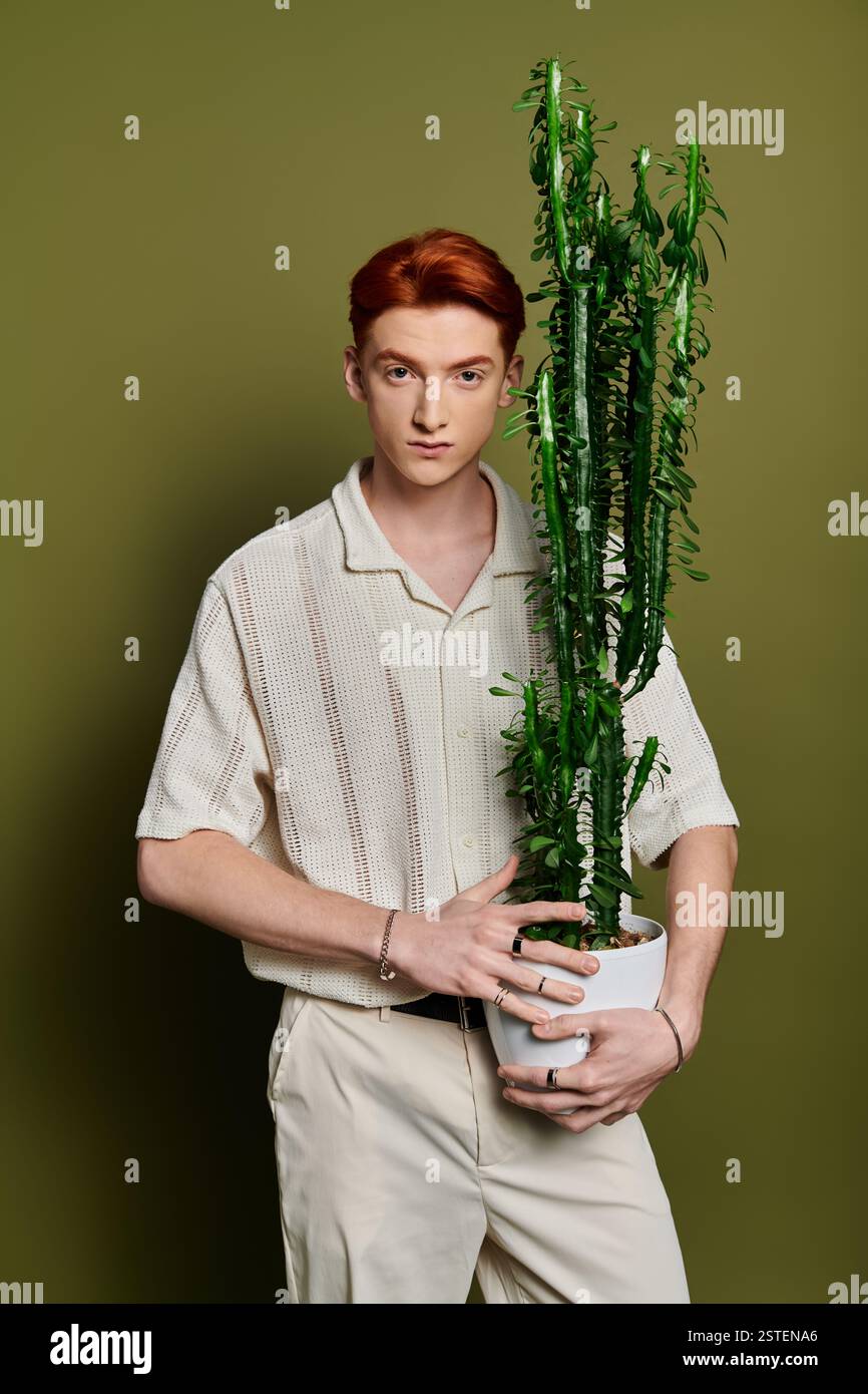 Young and handsome man stands confidently with a tall cactus, showcasing emotion and style. Stock Photo