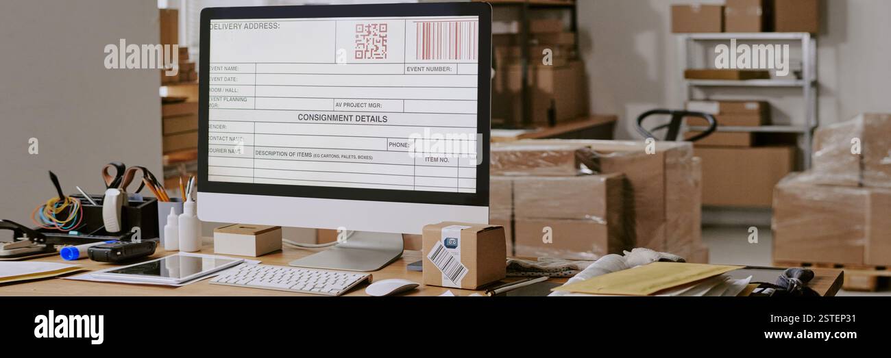 Close-up of computer monitor showing shipping label in busy office environment with various packaging materials and office supplies organized around work desk Stock Photo