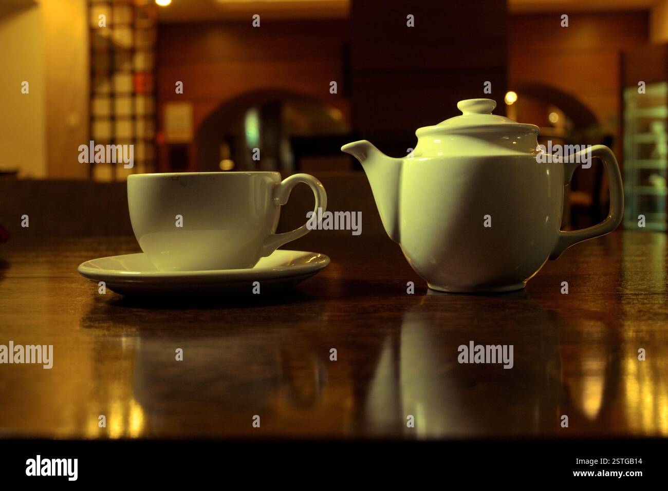 Tea time. White teacup and teapot on the wooden table in dark room, side view Stock Photo