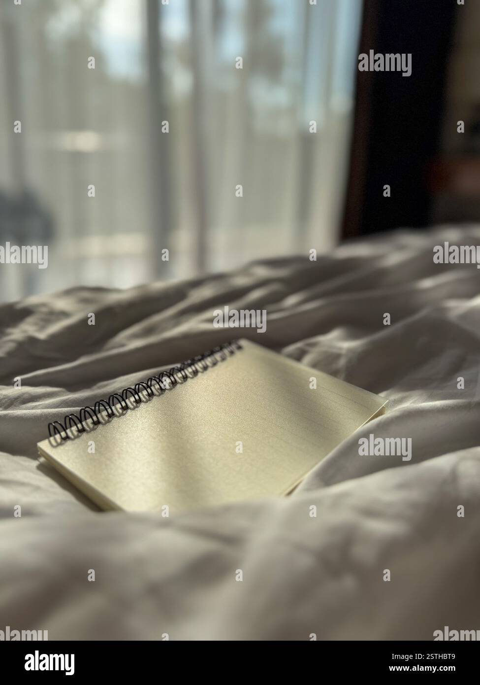 Hotel Room with Window, Soft Light, and Notebook on the Bed A room bathed in soft light filtering through sheer curtains. The atmosphere is peaceful, - Smartphone Captured Stock Image