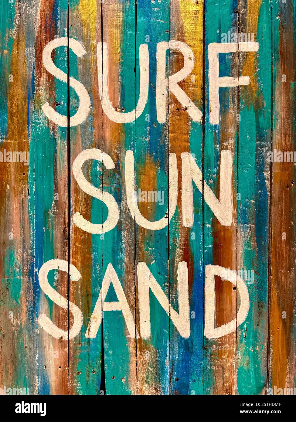 Vibrant and rustic artwork featuring the words ‘Surf Sun Sand’ painted in white on a textured wooden board. The turquoise, gold, and brown tones evoke - Smartphone Captured Stock Image