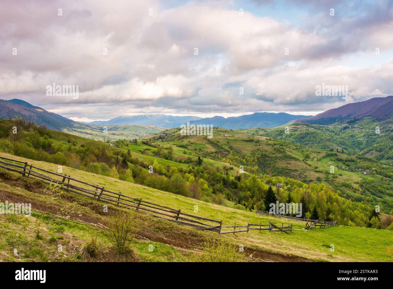 mountain landscape in spring. meadow on the hillside. countryside scenery with rolling hills. sky with clouds in evening light. weather change Stock Photo