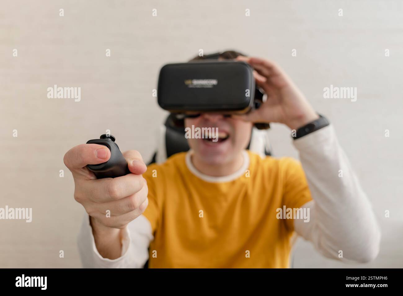 Young man in VR glasses playing video game with joystick, siting on the couch while having virtual reality experience Stock Photo