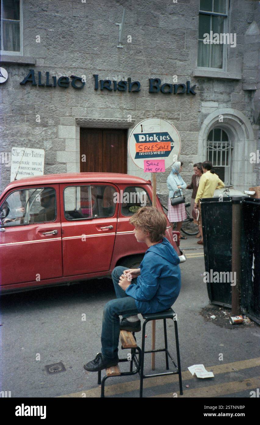 Boy sitting on a stool holding an advertising sign on an unknown High ...