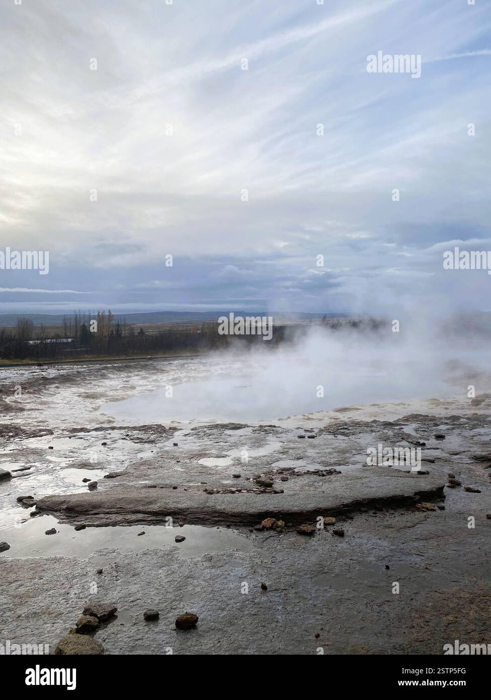 A rugged geothermal area with steam rising from rocky ground, showcasing the interplay of natural features and atmospheric conditions Stock Photo
