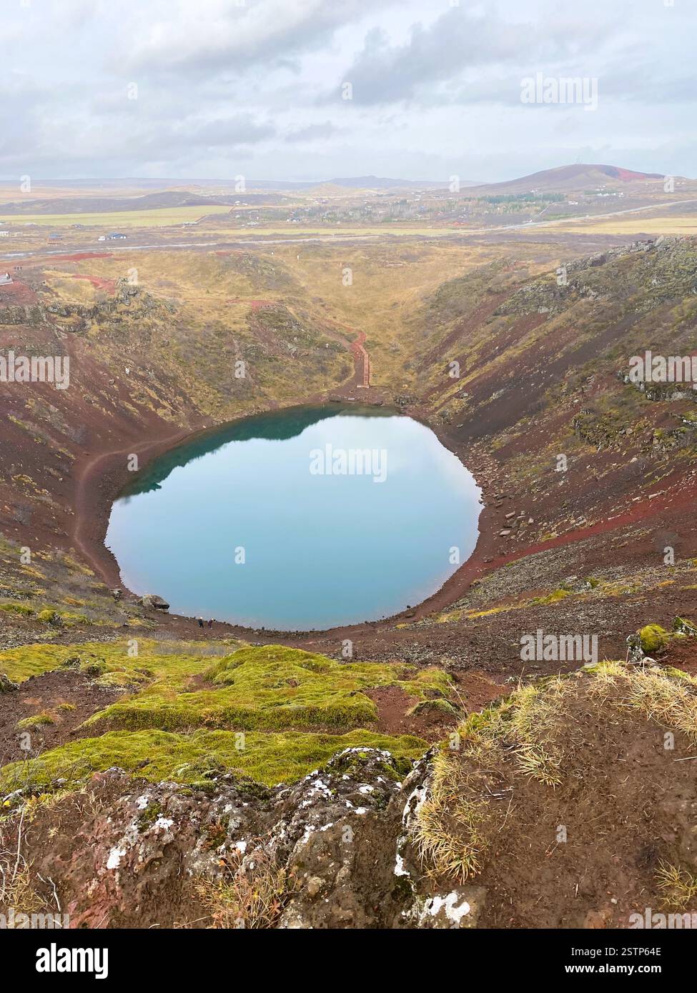 A stunning volcanic crater lake with vibrant blue water, steep reddish-brown walls, and a serene atmosphere, inviting exploration along its winding pa Stock Photo