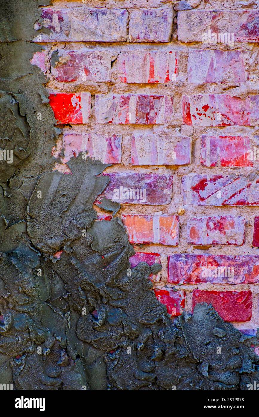 Old red brick wall half covered with cement plaster Stock Photo