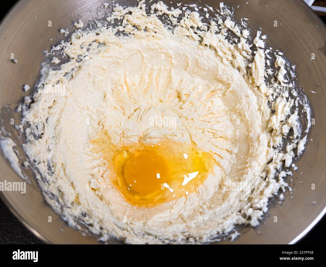 Beating butter, sugar and eggs in a grey metal bowl. The process of making cake and cookies by mixing butter, eggs and sugar. Close-up of an egg in cr Stock Photo