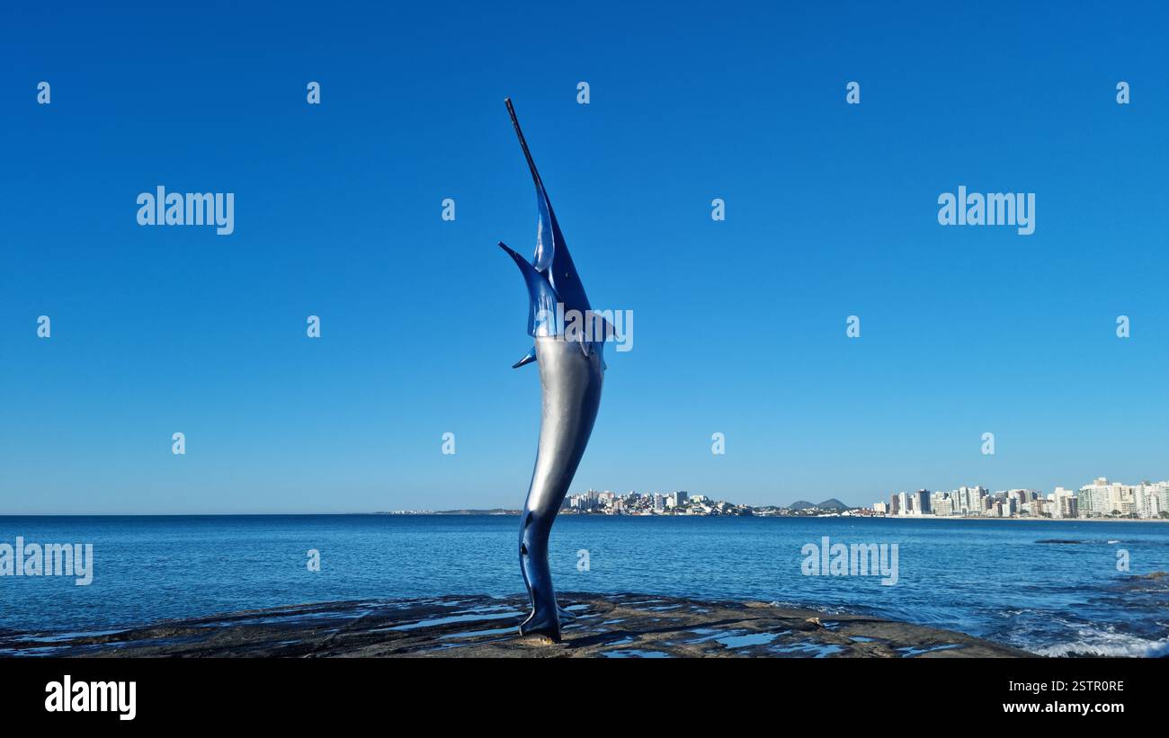 This striking image features a towering marlin sculpture standing proudly on a rocky shoreline, appearing as if it is leaping out of the sea. - Smartphone Captured Stock Image