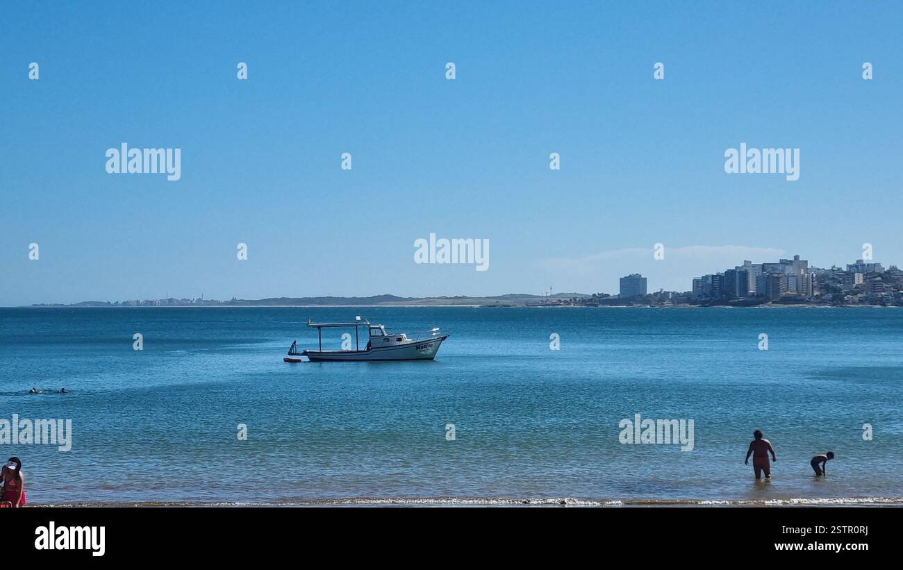 This serene image captures a picturesque beach scene with a fishing boat gently floating on the calm, crystal-clear waters. - Smartphone Captured Stock Image