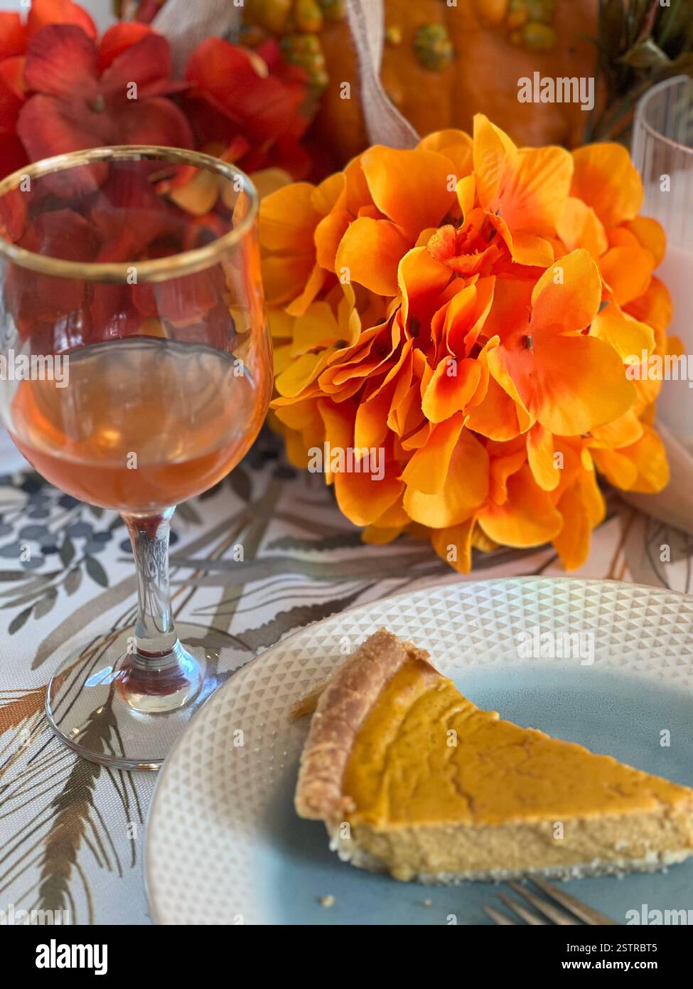A slice of tradition: pumpkin pie on a blue and white ceramic plate, paired with apple cider and autumn blooms.' - Smartphone Captured Stock Image