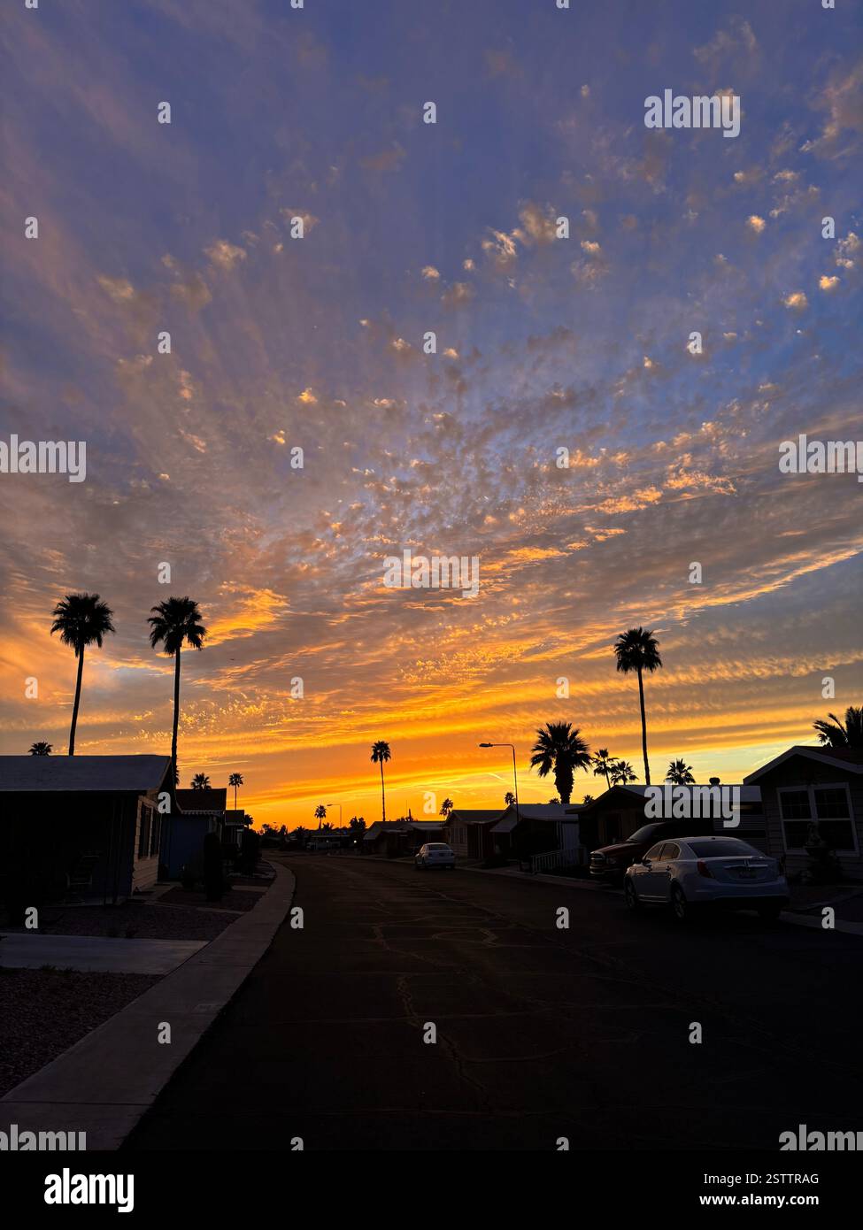 bright orange and indigo blue with spotty clouds above small arizona neighborhood in array of colors such as orange, red, purple, blue, and yellow - Smartphone Captured Stock Image
