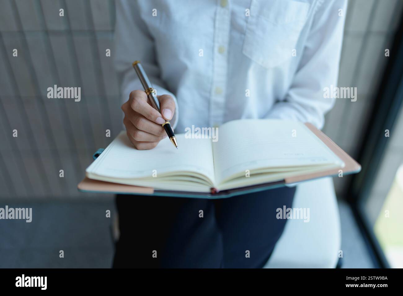 Person concentrating while writing in a book with a pen in a cozy study environment. Stock Photo