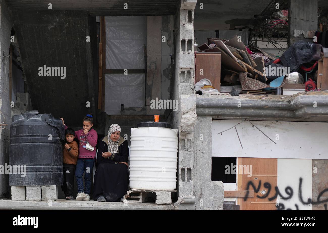 A Palestinian woman and two children sit in a partially standing home ...