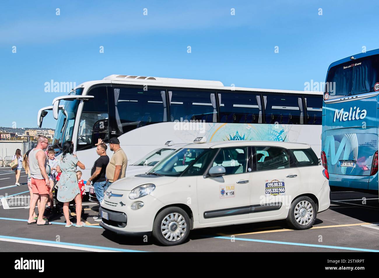 Catania. Italy - February 20, 2025: A typical tourist transportation scene in Catania, Sicily, with a white taxi and a white tourist bus parked in a b Stock Photo