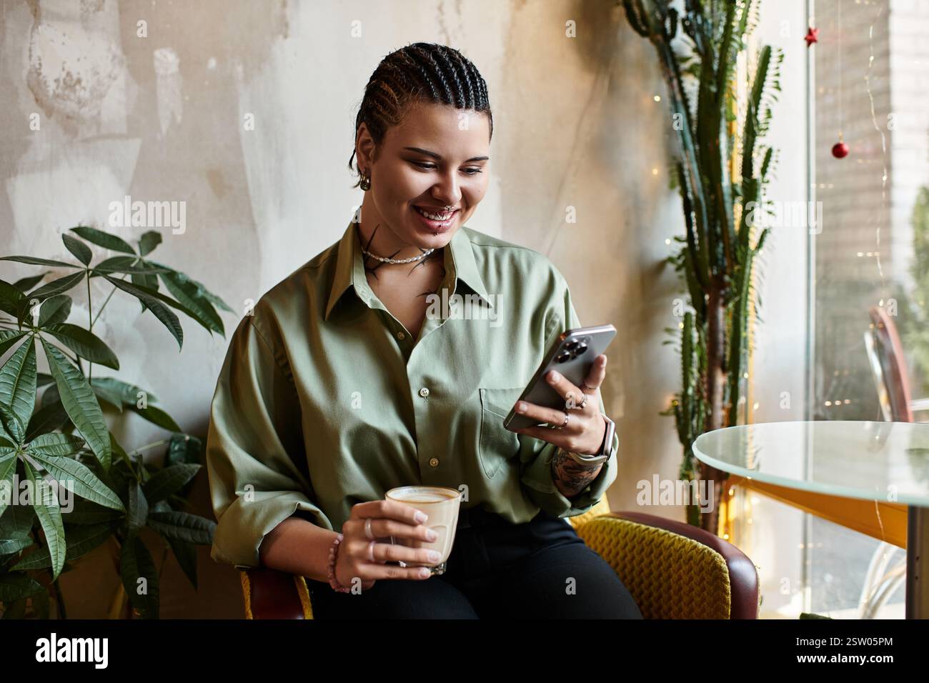 Smiling young woman sips coffee while browsing on her smartphone in a lively cafe. Stock Photo