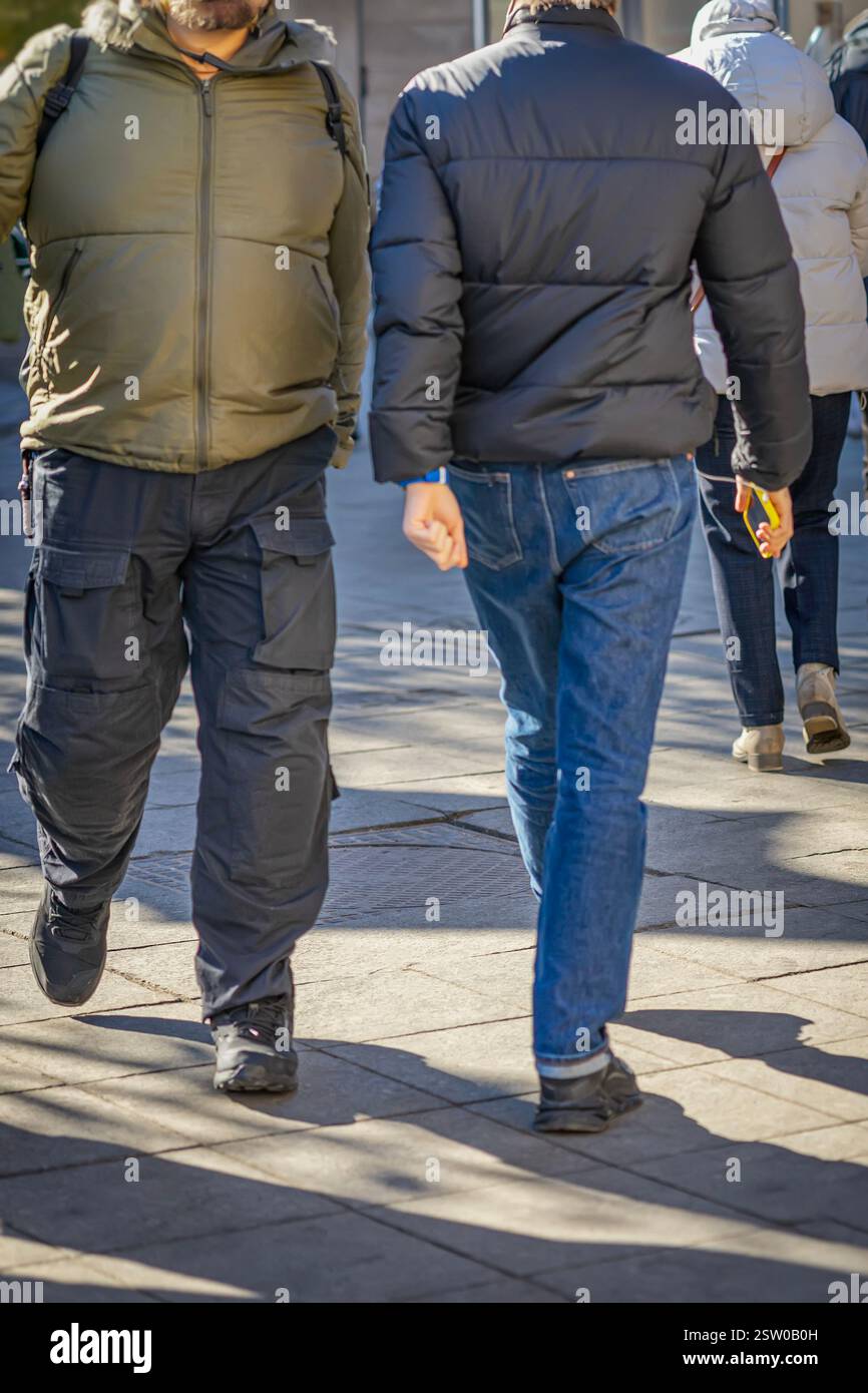 Two men in winter jackets walking on city street, one holding phone ...