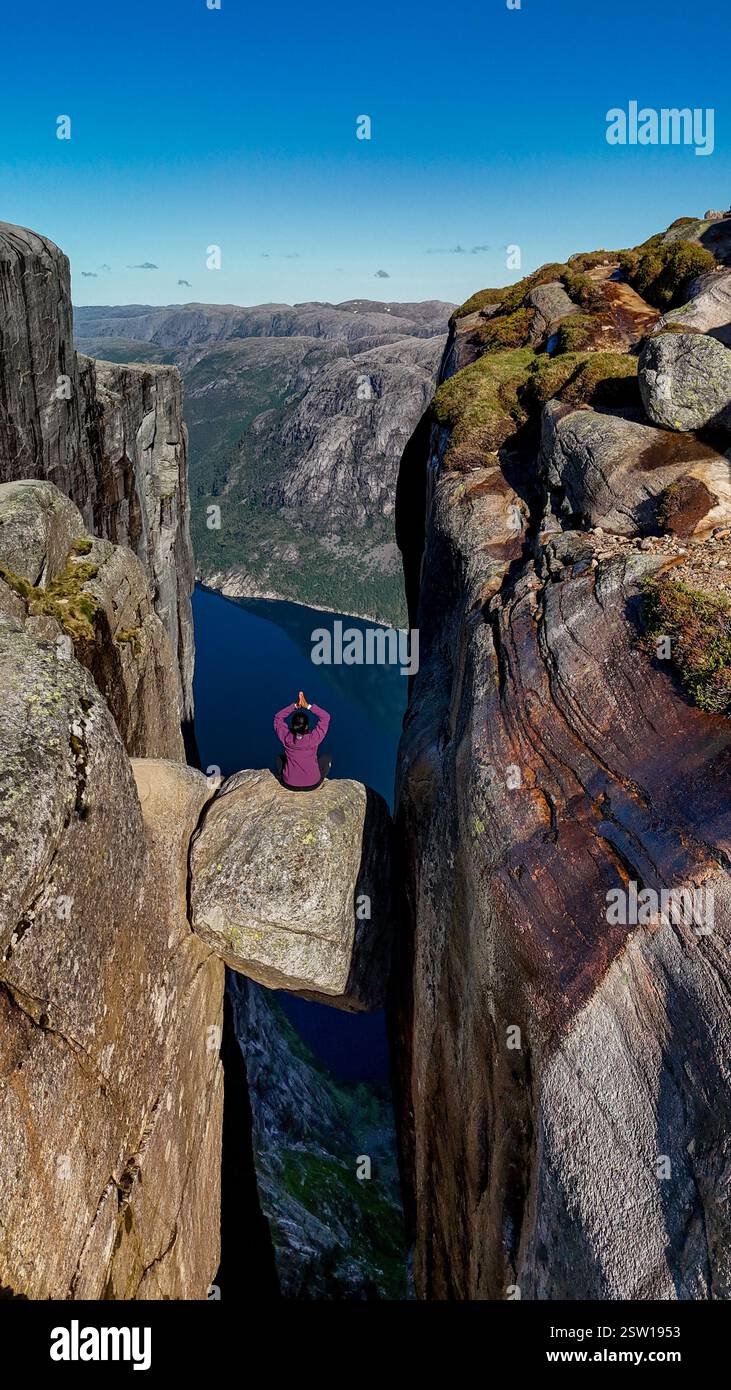 A lone adventurer stretches out atop the iconic Kjeragbolten cliff ...