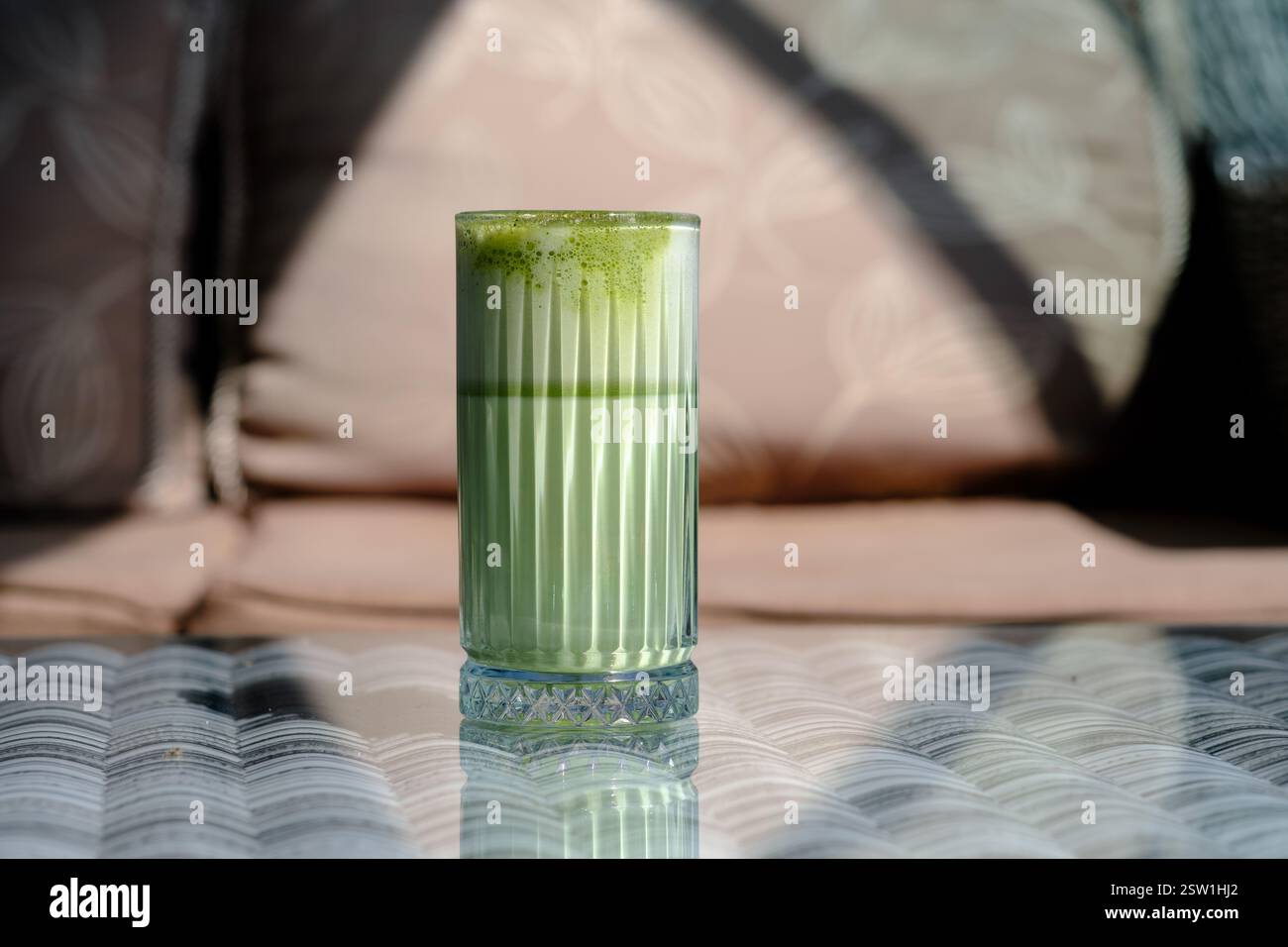 A refreshing green tea latte sits on a table bathed in sunlight Stock Photo