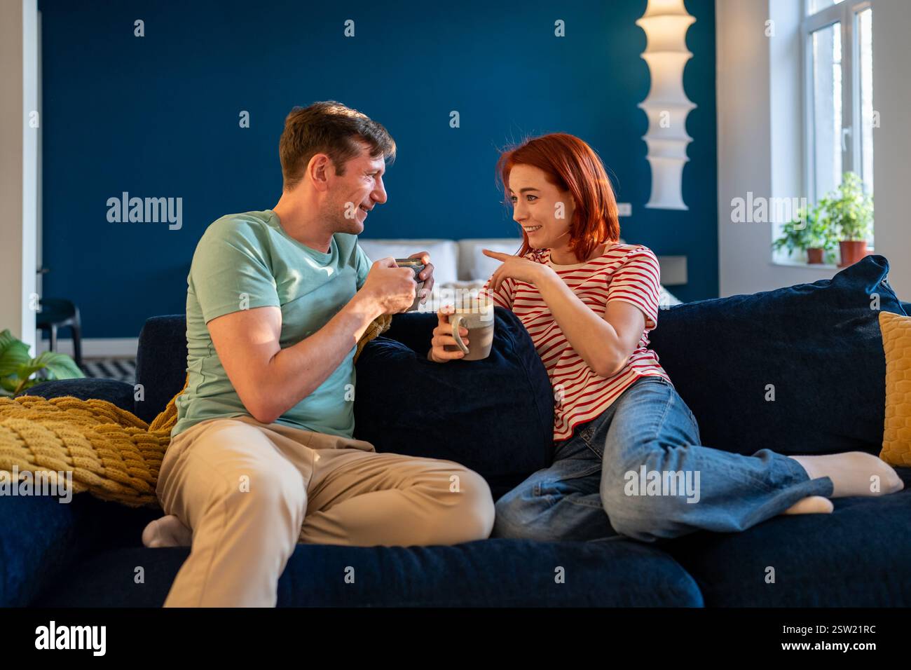 Happy relaxed couple drinking coffee or tea while resting together at home, enjoying weekend morning Stock Photo