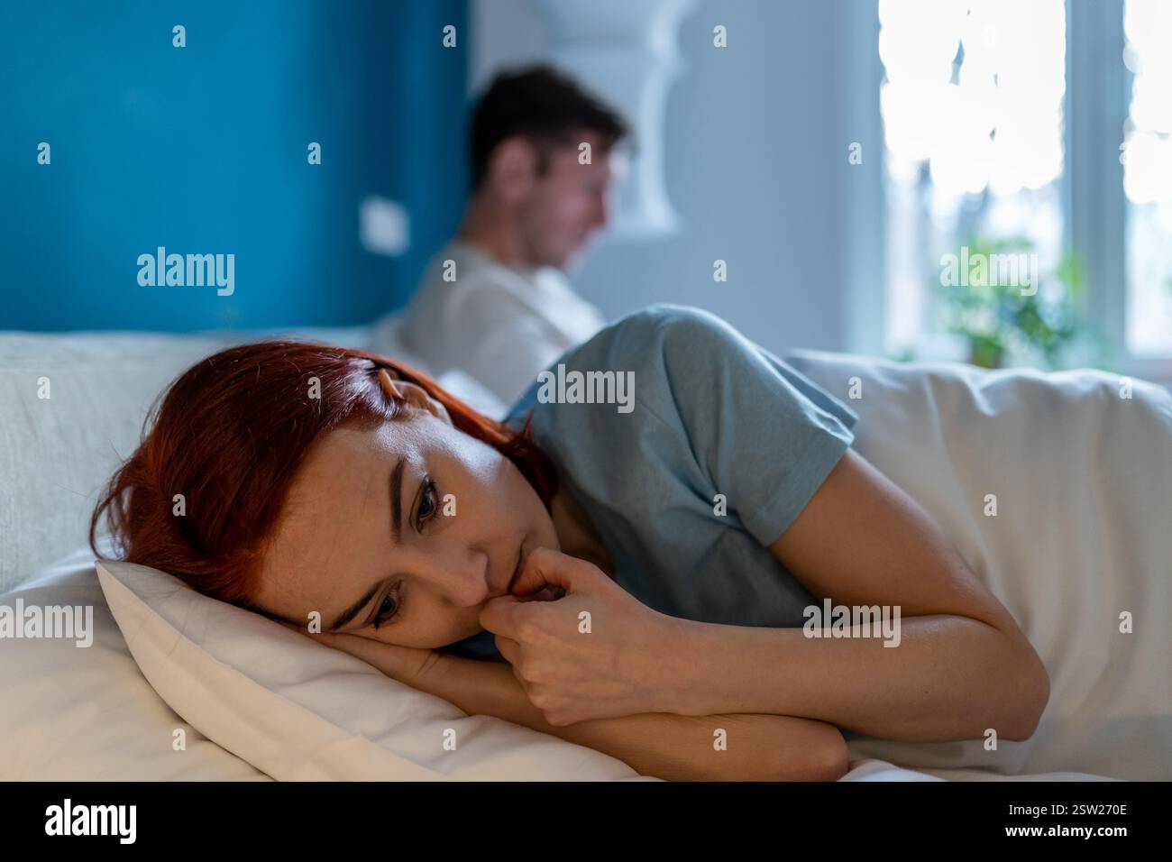 Upset wife lies with her back to husband. Man with disinterested look ...