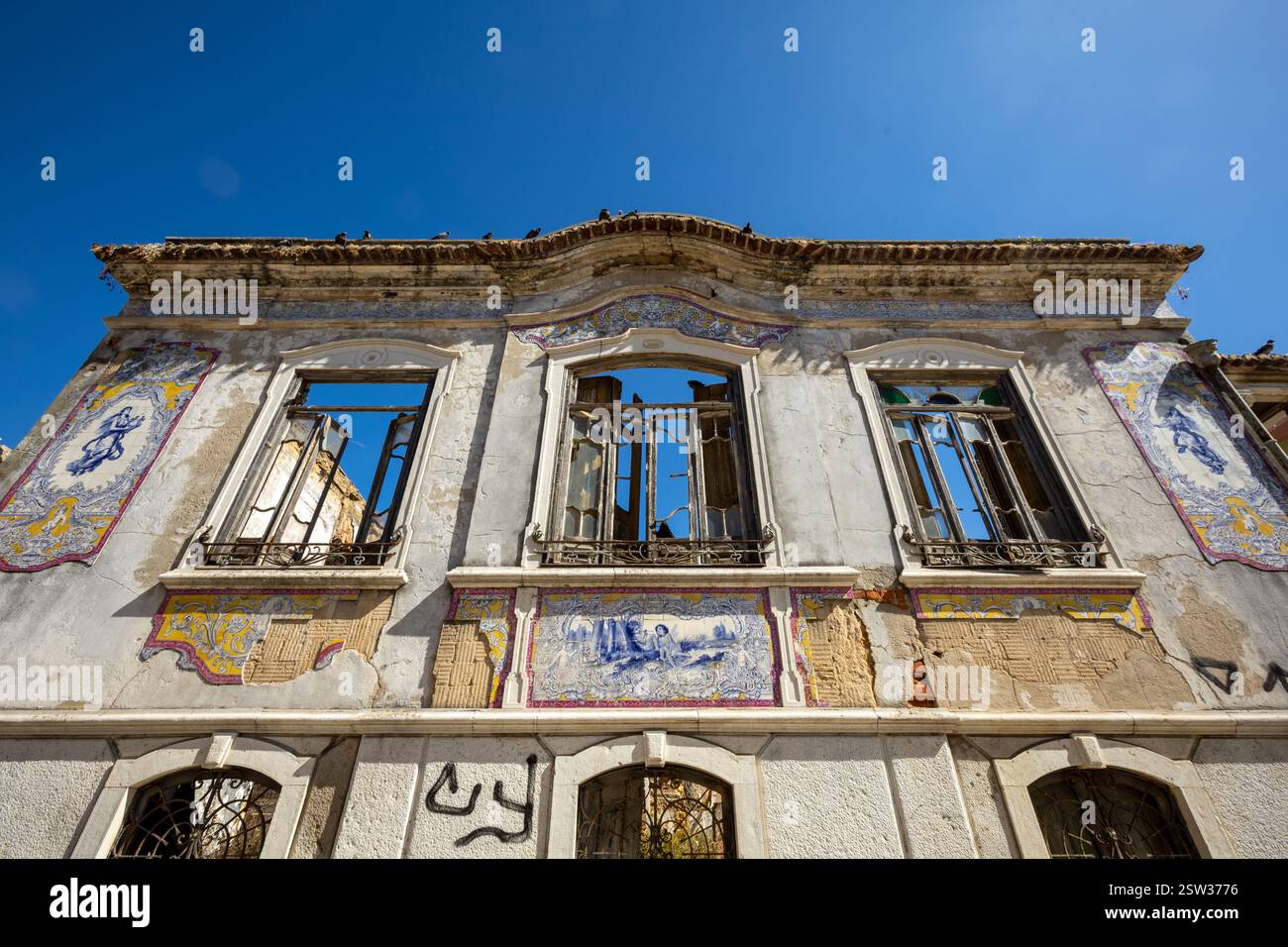 Old abandoned house. decorated with Portuguese tiles. Boken windows and a blue sky with pigeons on the ornaments. Ancient building, European city. Stock Photo