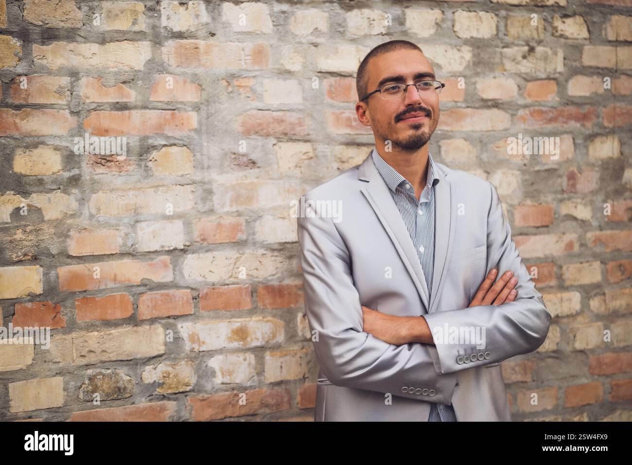 Portrait of young businessman who is standing in the front of brick wall, looking away and thinking. Stock Photo