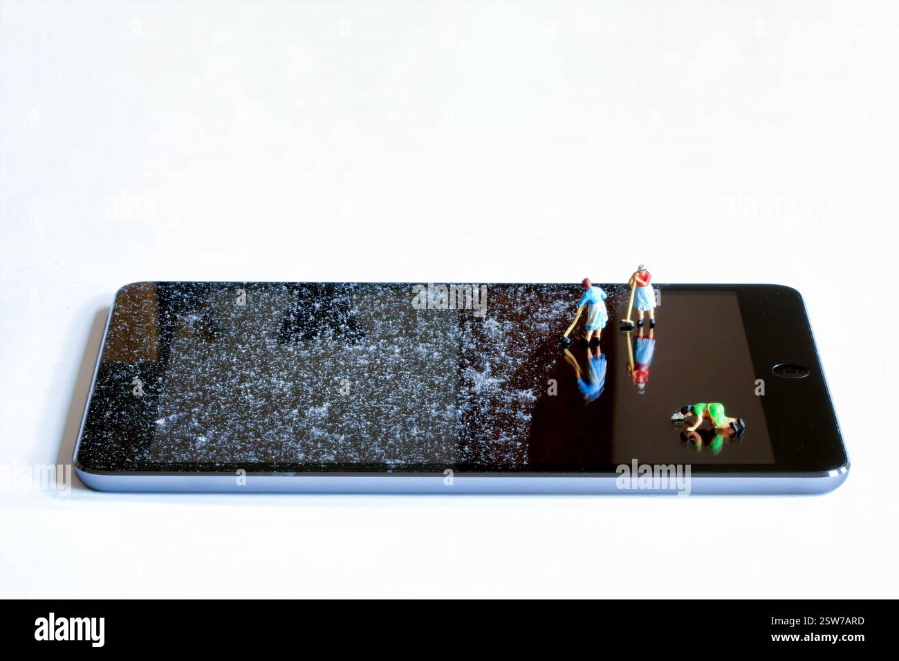 UK: Small 00 gauge tiny cleaning woman are shown cleaning a very dusty ipad or tablet screen. Miniature people cleaning an ipad screen Stock Photo