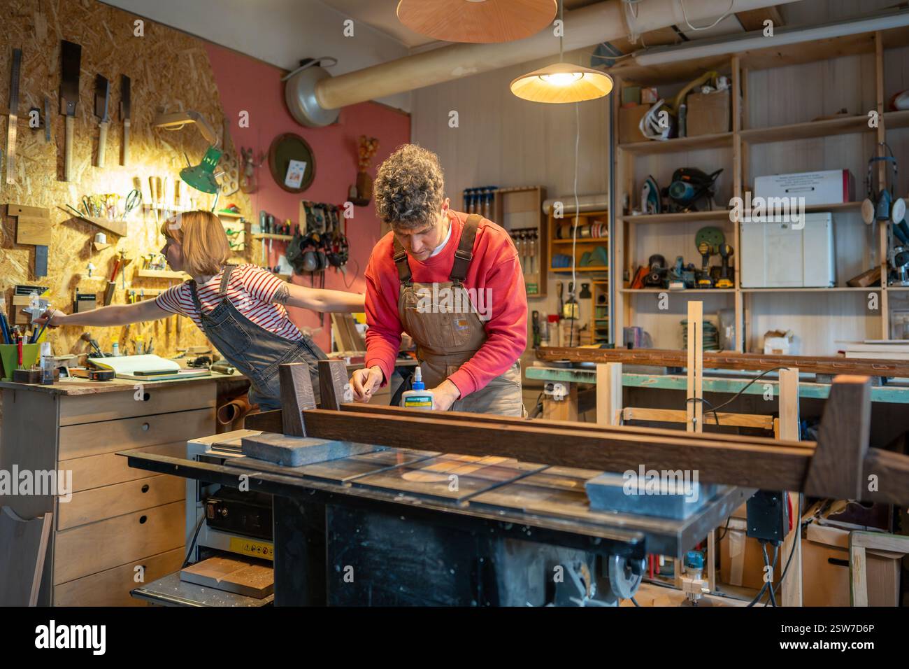 Artisan collaborating with apprentice assistant, constructs bed frame from solid wood in workshop Stock Photo