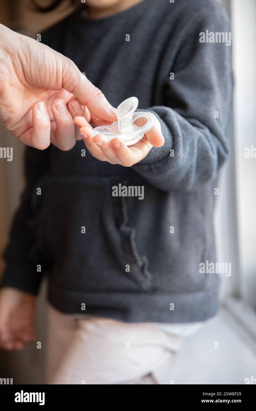 At home, a child hesitates as an adult gently takes a worn pacifier ...