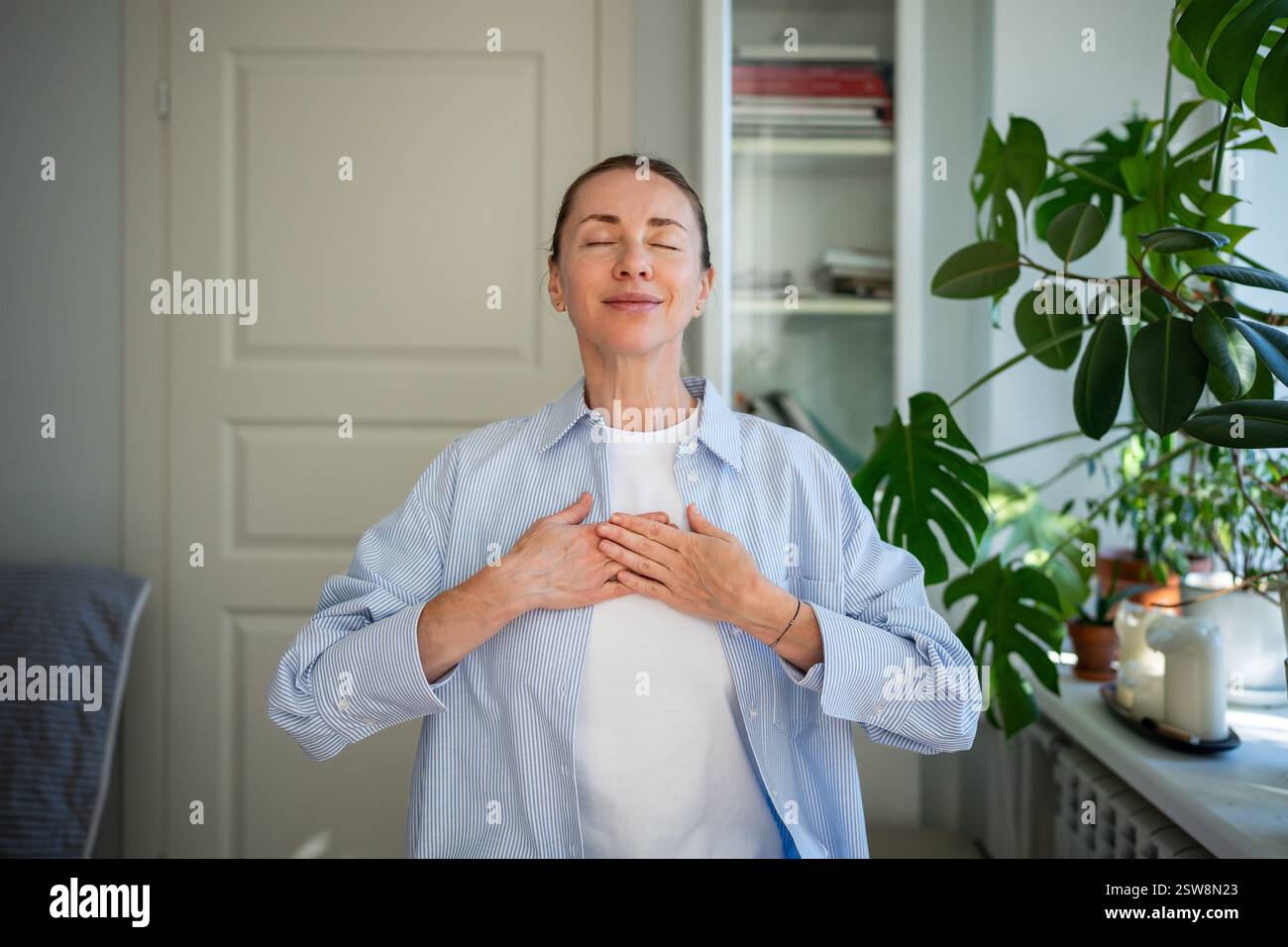 Relaxed smiling woman meditates with hands on chest, practice breathing exercises at home. Self care Stock Photo