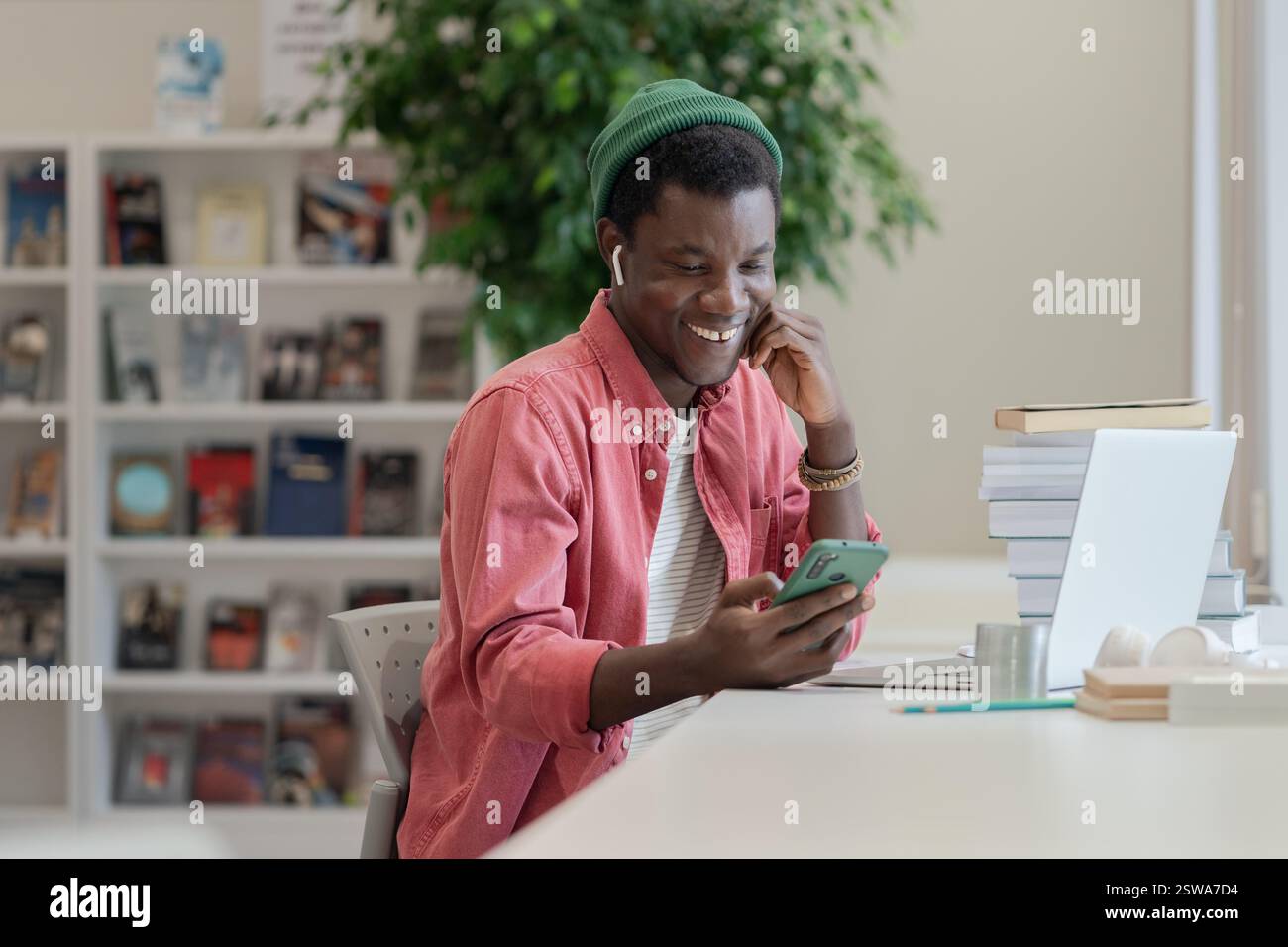 Happy African American student guy using mobile device while studying in library Stock Photo