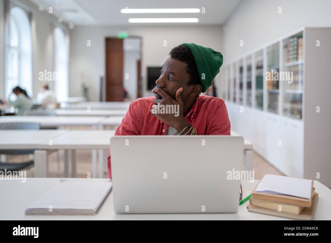 Pensive Black student man looking into distance while studying in library, disinterested in study Stock Photo
