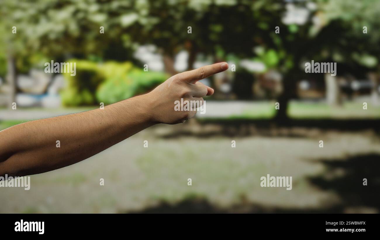 Man pointing hand outdoors on a city street, highlighting a focused gesture against a blurred urban background, suggesting direction or indication in Stock Photo