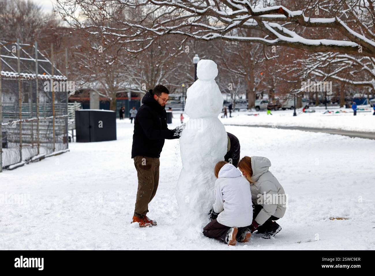 Several adult persons collaboratively build a snowman in Boston Commons, Boston, Massachusetts Stock Photo