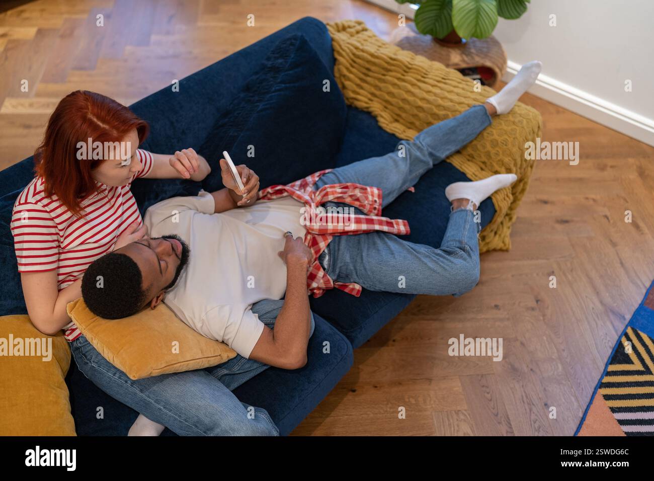 Young interracial couple using smartphone while resting on weekend at home Stock Photo