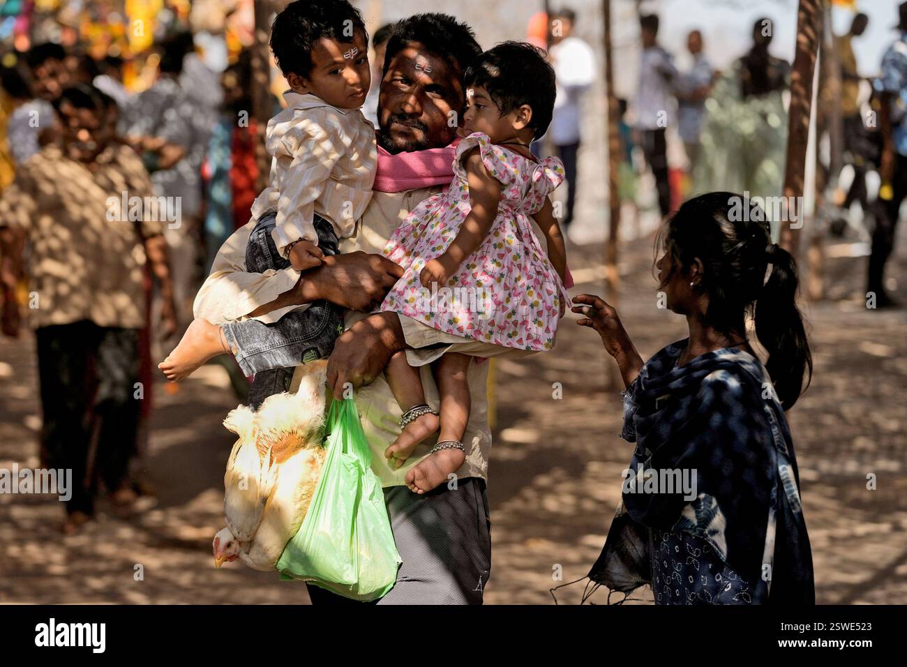 A devotee holds a live chicken while carrying two young children in his ...