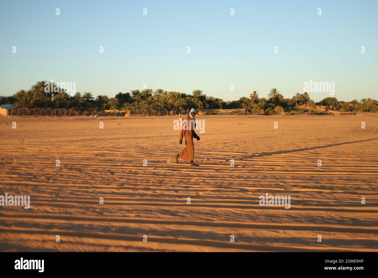 A man walks through sand with palm trees in the distance in Chinguetti