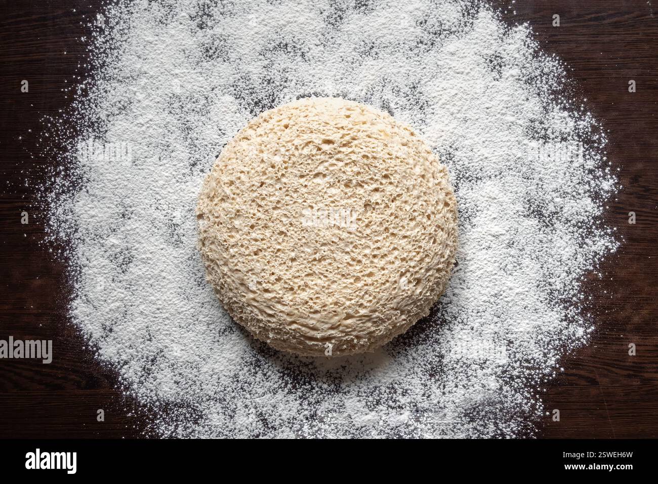 Round piece of yeast-free dough on a floured dark table. Cellular ...