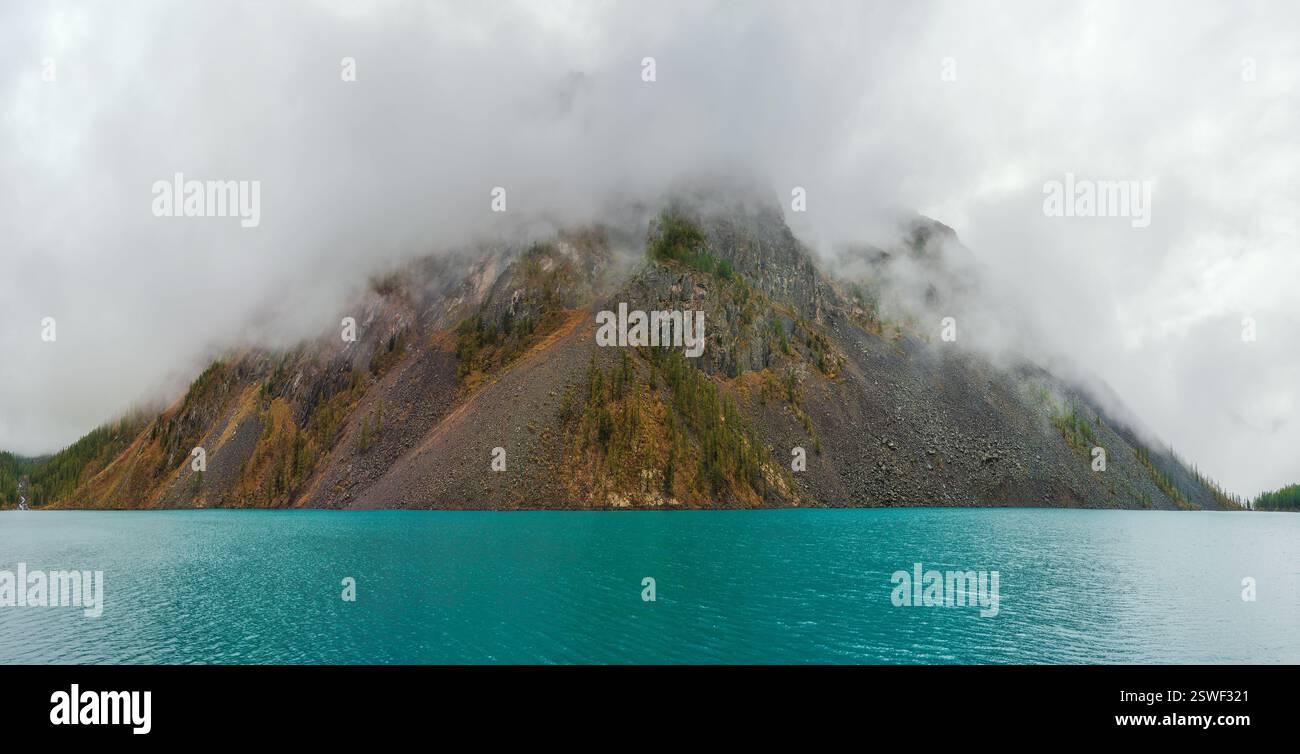 Panorama of a mysterious island in the fog. Alpine tranquil landscape at cool early morning. Ghostly atmospheric scenery. Stock Photo