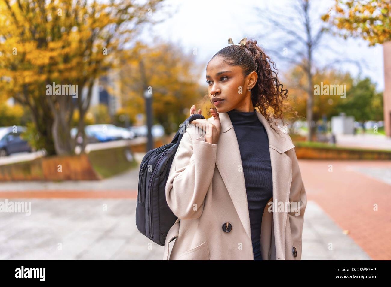 Elegant african american young businesswoman wearing trench coat carrying hand bag in the city in autumn Stock Photo