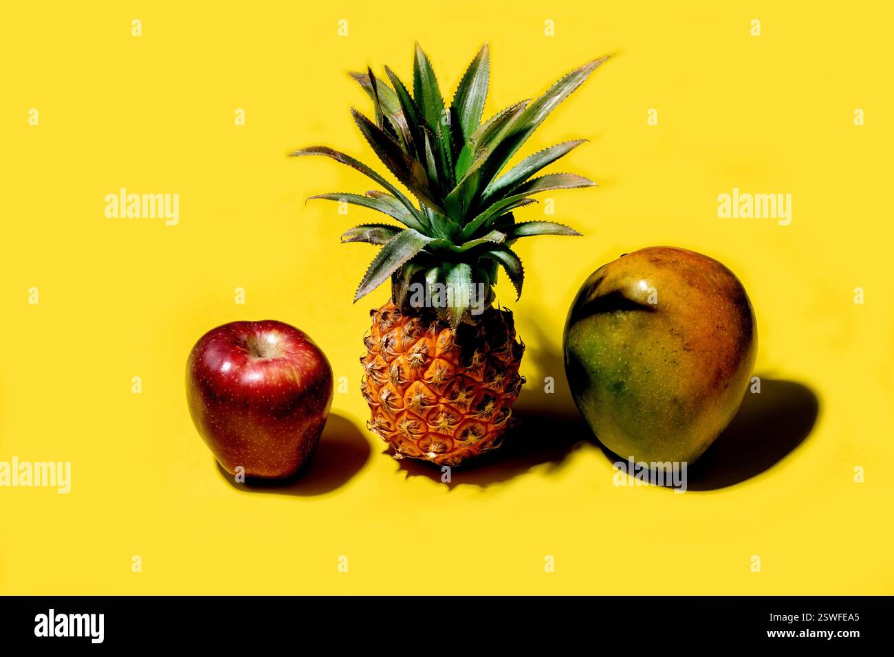Mini pineapple, mango and apple on a solid yellow background Stock Photo