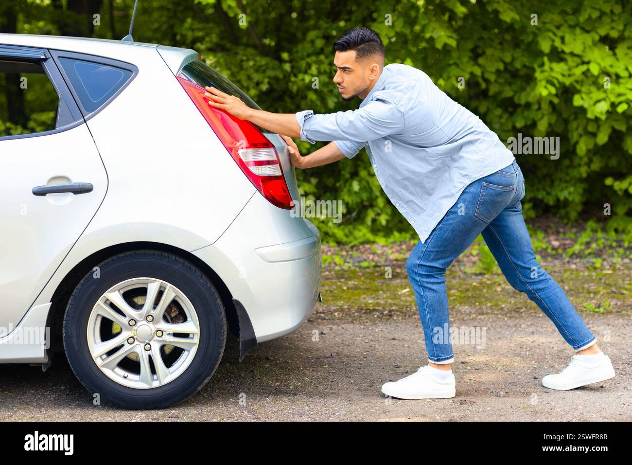 Arab guy pushing broken car, side view Stock Photo